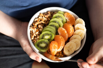 Traditional breakfast plate. Granola, banana, kiwi and nuts in a bowl in the hands of teenagers.