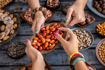 A bowl of pistachio at the hands of two woman and assorted nuts at the background