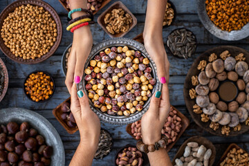 A bowl of hazelnuts at the hands of two woman and assorted nuts at the background