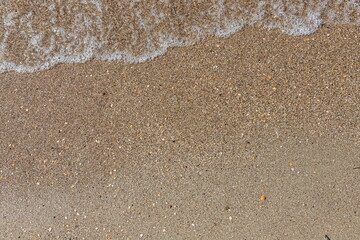 Close-up of sea foam on the sand beach with summer sunlight