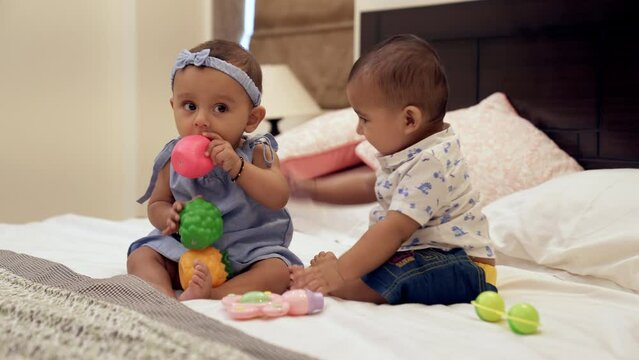 A little boy and a cute girl relaxing together while sitting on the bed at home. Happy siblings playing together with colorful toys - social-emotional skills  bonding and relationships  sharing  twins