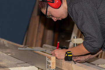 Young woman carpenter taking measurement of a wooden plank