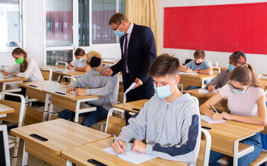 Portrait of diligent schoolboy wearing protective face mask sitting in class working with...
