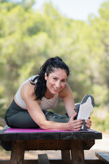 Happy caucasian adult woman stretching her leg on a picnic table in park