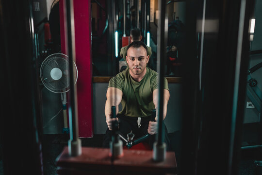One man young adult caucasian male bodybuilder training back on the cable crossover exercise machine in the gym wearing shirt dark photo real people copy space front view