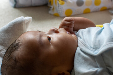 A Japanese Asian infant baby lying down on the white carpet looks at his mother with blue clothes