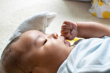 A Japanese Asian infant baby lying down on the white carpet looks at his mother with blue clothes