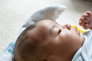 A Japanese Asian infant baby lying down on the white carpet looks at his mother with blue clothes
