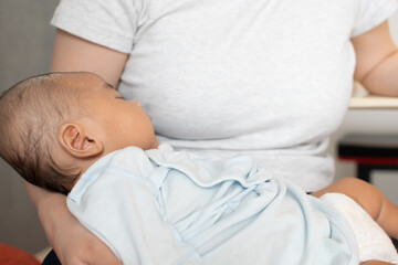 A Japanese Asian infant baby is sleeping on his mother's arm