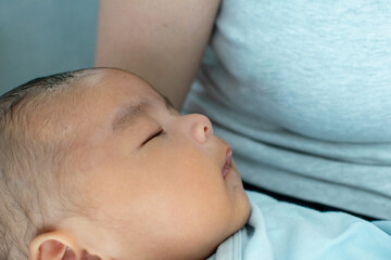 A Japanese Asian infant baby is sleeping on his mother's arm