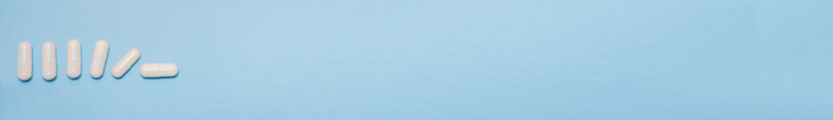 Banner white tablets or capsules lie on a light blue background and gradually fall with space for text. Useless pharmaceutical, Covid-19 or coronavirus