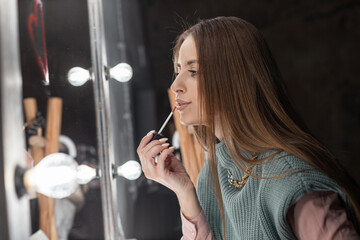 Fashionable beautiful young woman in stylish vintage clothing makes make-up near the mirror and...