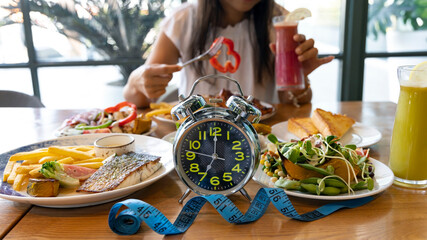 Selective focus of  Alarm clock with woman eating a healthy food as Intermittent fasting,...