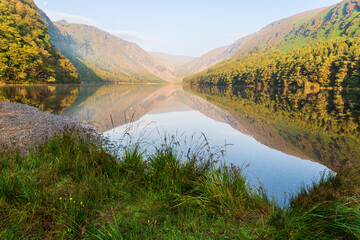 Obraz premium Lake in the mountains. Glendalough Upper Lake on a calm day reflecting the Glenealo Valley landscape, in Wicklow, Ireland.