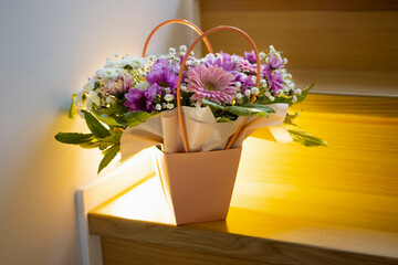 A composition of flowers in a festive box stands on the stairs with lighting. A gift for a beloved woman