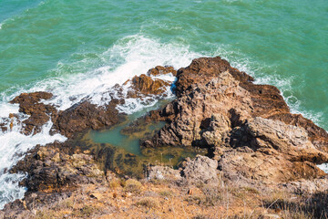 high angle shot of waves crashing against a rock formation in the sea