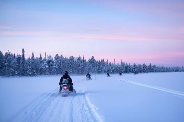 Tuinposter Snowmobiling on the frozen lake at sunset at Torassieppi, Lapland, Finland © Matthew