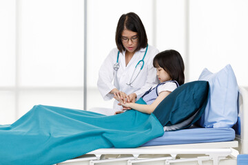 Obraz premium Asian professional friendly female doctor in white lab coat and stethoscope standing smiling to young girl patient lay down on bed in hospital wardroom