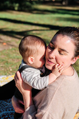 Fototapeta premium Young woman playing with her baby in a public park on a sunny day