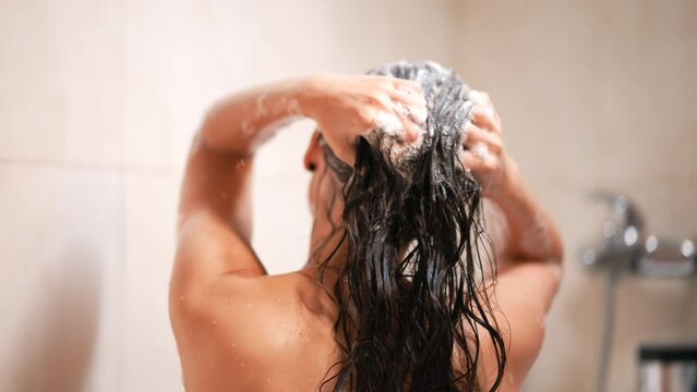 Woman takes a shower and shampoos her hair in the bathroom