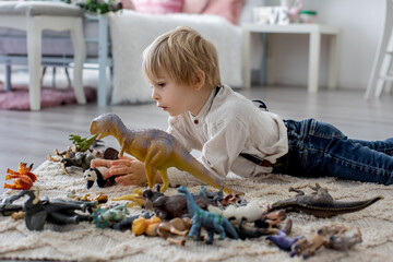 Cute toddler preschool child, blond boz, plazing with animals and dinosaurs