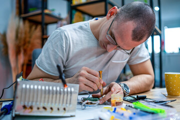 The young master electronics engineer checks, repairs and finishes the motherboard he was given to repair. He uses his tools and works in a home environment.
