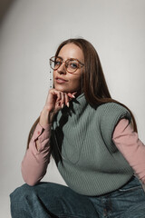 Fashion portrait of pretty glamour girl with vintage glasses in stylish knitted clothes sits and poses in studio