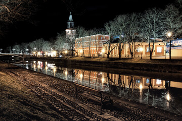 Fototapeta na wymiar The atmospheric Aura River in Turku, Finland flows peacefully at night in early spring. Turku Cathedral, built in the Middle Ages, can be seen illuminated in the background.