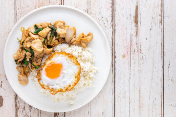 Khao Pad Ka Prao Gai Kai Dao, Thai food, streamed rice topped with basil stir fried chicken and fried egg in white ceramic plate on white old wood texture background with copy space for text, top view