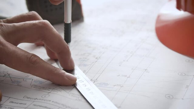 Process of making adjustments to working drawings. Hand of an engineer uses a ruler and a mechanical pencil to make changes to the design documentation. Ruler pencil tape measure and safety helmet.
