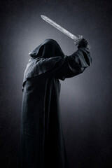 Warrior with hooded cape and medieval sword over dark misty background