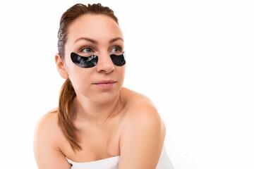 young woman with black cosmetic patches under her eyes against a white wall