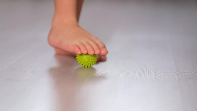 Flat feet physical therapy. foot step on massage ball to relieve Plantar fasciitis or heel pain. Little boy massaging trigger points on foot. Flat feet correction exercise. Slow motion