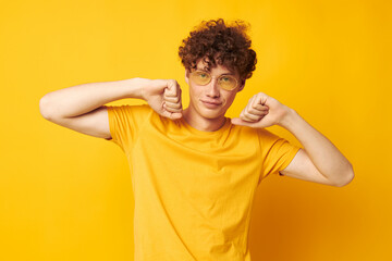 portrait of a young curly man yellow t-shirt glasses fashion hand gestures isolated background...