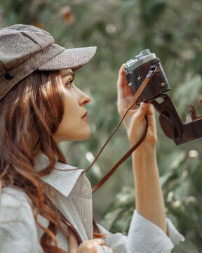 Portrait of a girl in profile in retro clothes takes pictures on a retro camera against the backdrop of nature.