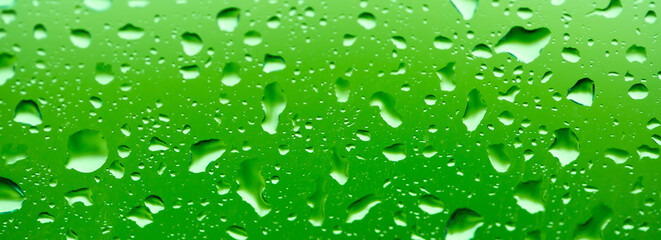 Rain outside the window. Water droplets on a car glass on a background of blue sky and green grass. Overcast. Wet clean nature, ecology