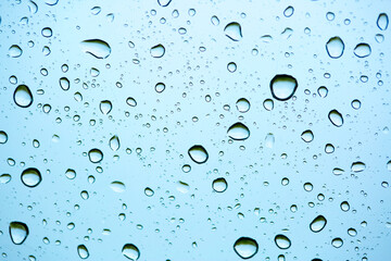 Rain outside the window. Water droplets on a car glass on a background of blue sky and green grass. Overcast. Wet clean nature, ecology