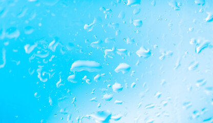 Rain outside the window. Water droplets on a car glass on a background of blue sky and green grass. Overcast. Wet clean nature, ecology