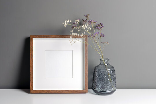 Blank square frame with passepartout mockup over grey wall with dry flowers decorations. Minimalistics style interior with artwork mockup.
