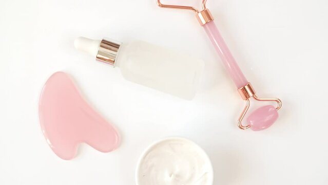 Rotation of pink quartz facial roller and glass bottle with gel, fluid and massage stone isolated on white background. The concept of natural cosmetic product and skin care. High quality 4k footage