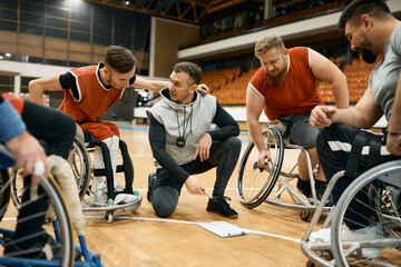 Fototapeta na wymiar Basketball players in wheelchairs and their coach planning strategy before the match on sport court.