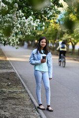 A young girl walks in the city park in the spring. Alley of blooming apple tree. 