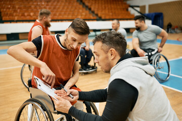 Basketball player in wheelchair and his coach planning game strategy on the court.