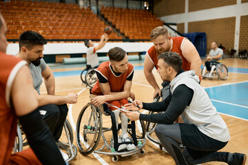 Basketball team with disabilities and their coach analysing game strategy during wheelchair basketball match.