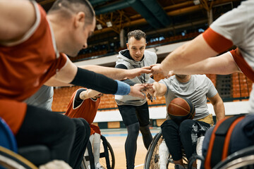 Wheelchair basketball team and their coach gather their hands in unity before the match.