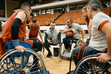 Coach of wheelchair basketball and his players with disabilities going through game strategy on the court.