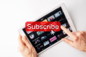 Subscribe now. Online video subscription red button. Internet service on laptop digital tablet blured technology background. Streaming video. Communication network.