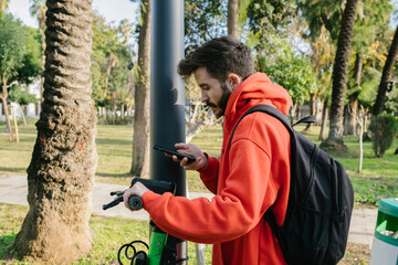 Electric scooter, Young man locks scooter for public use on lamppost, Scanning qr code from mobile...