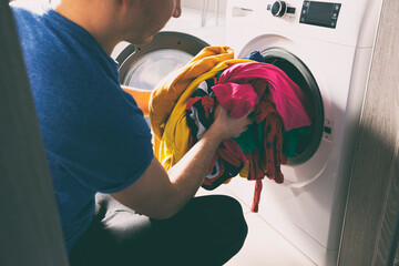 Man loading the washer dryer with clothes - obrazy, fototapety, plakaty