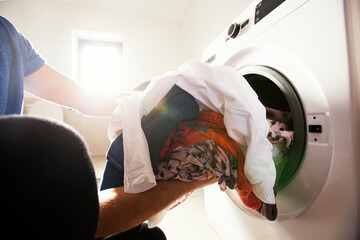 Man loading the washer dryer with clothes with different color and type